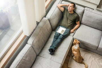 Man at home with tablet on the couch with dog beside him