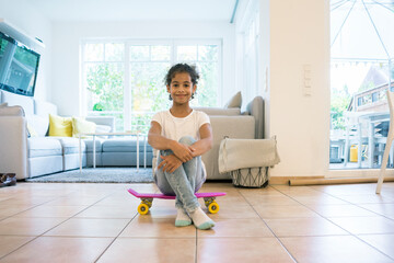 Little girl sitting on skateboard, looking proud