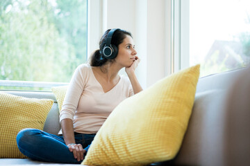 Woman sitting alone on couch, listening music with headphones