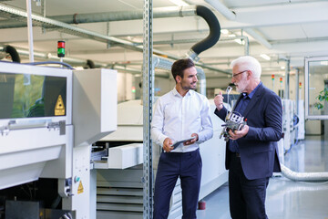Senior manager discussing machine part with engineer by machinery at factory