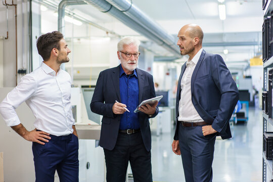 Senior manager with colleagues discussing over digital tablet while standing at illuminated factory