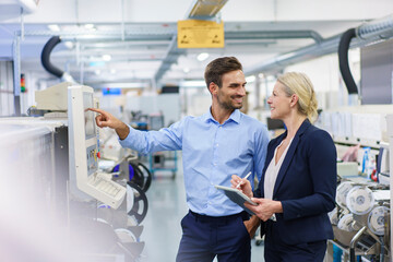 Smiling male technician looking at businesswoman while standing by machinery at illuminated factory