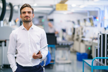 Confident young businessman holding digital tablet while standing at illuminated factory