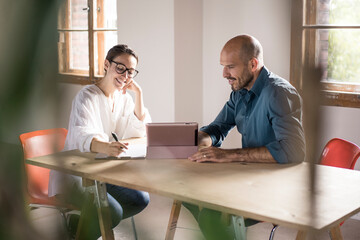Businesswoman writing in notepad while sitting by man using digital tablet at office
