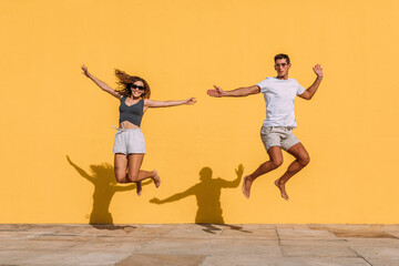 Fototapeta na wymiar Young couple jumping in front of a yellow wall