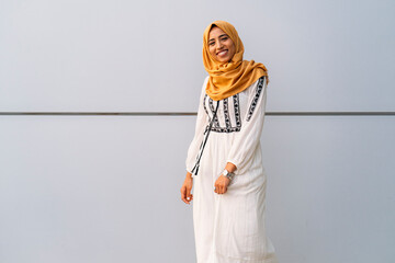Young muslim woman wearing yellow hijab and walking in front of a white wall - Powered by Adobe