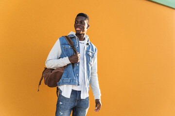 Young man carrying backpack while standing against yellow wall on sunny day