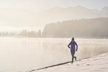 Germany, Bavaria, Lake Walchen, woman jogging in winter