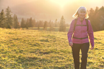 Portrait of senior hiker walking across alpine meadow at sunset