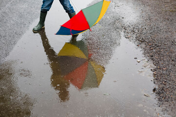 Little boy with umbrella and rubber boots standing in a puddle, partial view