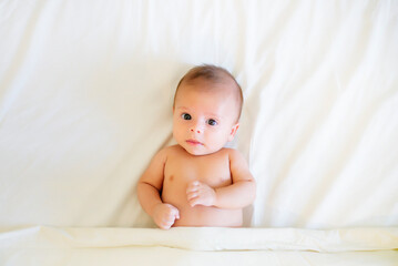 Portrait of baby boy lying on white bed sheet