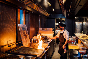 Chef wearing protective face mask preparing grill in restaurant kitchen