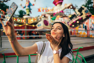 Young woman blowing kiss while taking selfie at amusement park 