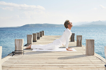 Mature man doing yoga exercise on jetty
