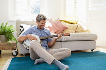 Man sitting on floor, playing the banjo - obrazy, fototapety, plakaty