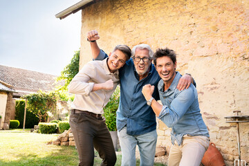 Portrait of three excited men of different age embracing and cheering in garden