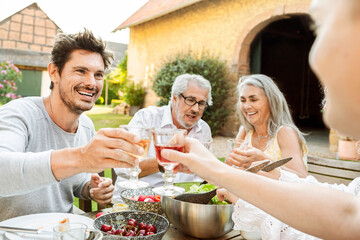 Happy family eating together in the garden, clinking glasses