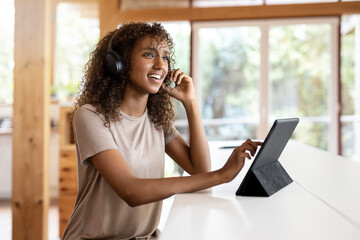 Businesswoman with digital tablet talking through headphones while sitting at home