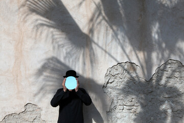 Morocco, Essaouira, man wearing a bowler hat holding mirror in front of his face at a wall