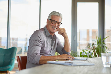 Portrait of smiling mature man using laptop on table at home