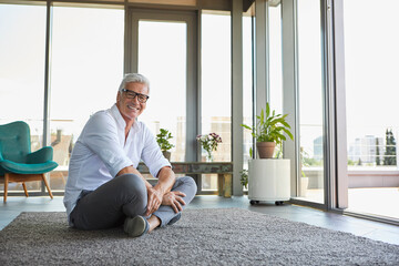 Smiling mature man relaxing sitting on carpet at home