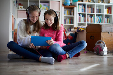 Siblings playing at home with their digital tablets, sitting on ground