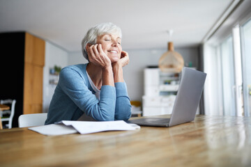 Thoughtful senior woman with hand on chin sitting at home