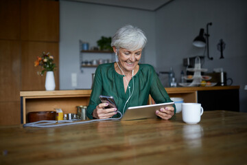 Senior woman listening to music while using smart phone and digital tablet at home
