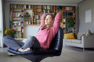 Mid adult woman with hands behind head relaxing on chair at home