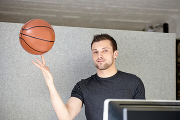 Young man working in office, balancing a basketball