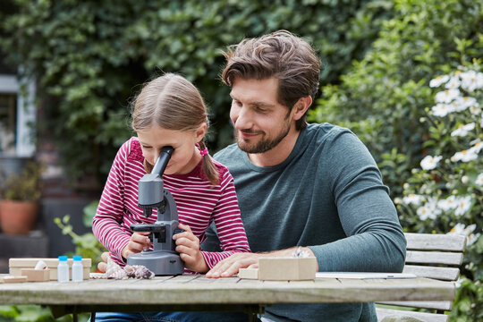 Father and daughter using microscope together at garden table
