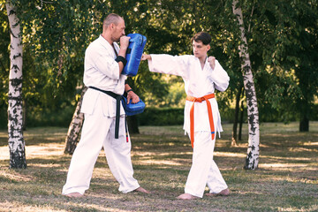 Teenage boy with instructor practicing karate at summer park
