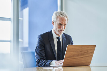 Confident businessman using laptop at desk in office