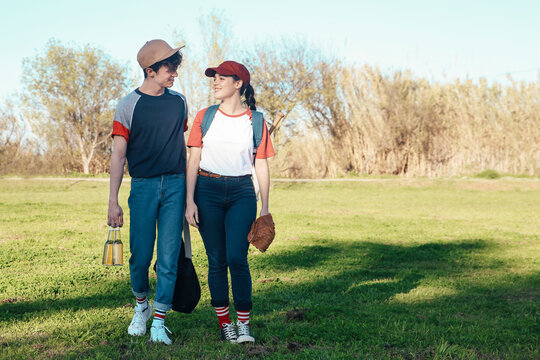 Smiling young couple with baseball equipment walking in park