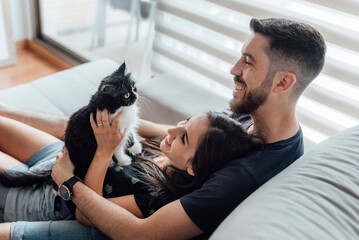 Happy couple spending leisure time with cat while sitting at home