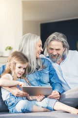 Grandparents and granddaughter sitting on couch, using tablet