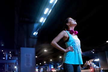 Young woman with pink headphones in modern urban setting at night