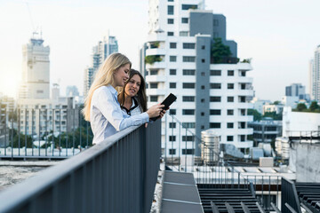 Two businesswomen talking on city rooftop, using digital tablet