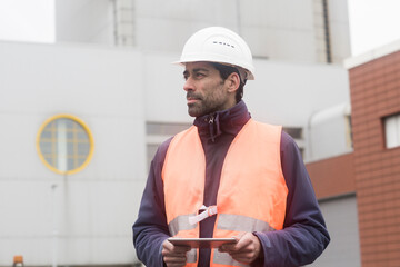 Man wearing reflective vest and hard hat holding tablet looking around
