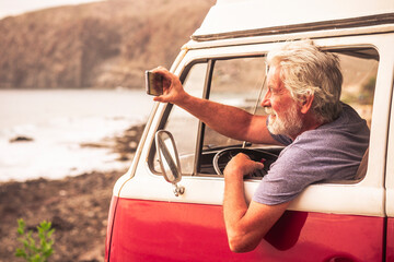 Senior man travelling in a vinatge van, taking pictures of the sea