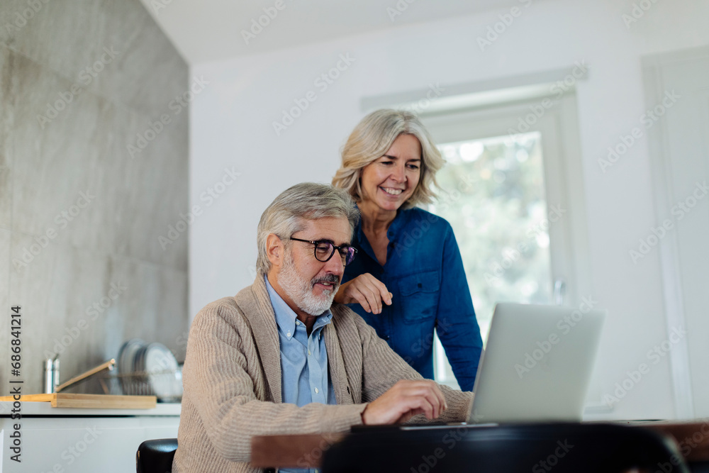 Wall mural mature man with wife using laptop on kitchen table at home