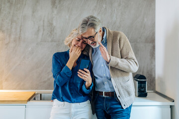 Mature couple using cell phone together in kitchen at home