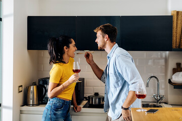Happy young couple cooking and drinking wine in the kitchen at home together - Powered by Adobe