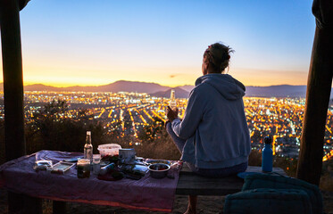 Chile, Santiago, woman drinking a beer in the mountains above the city at sunset
