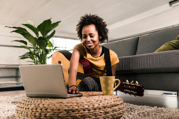Smiling young woman at home with guitar and laptop