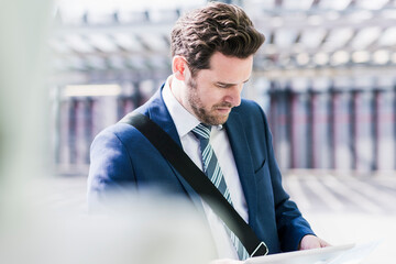 Businessman standing on parking level, reading on digital tablet