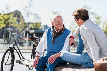 Senior man and adult grandson talking on a bench - obrazy, fototapety, plakaty