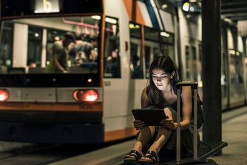 Portrait of young woman waiting at tram stop by night using tablet