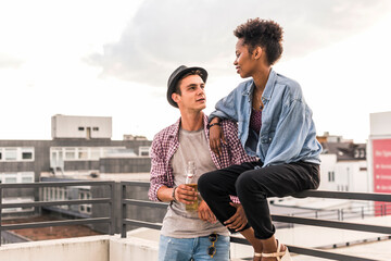 Young couple with beer bottles socializing on rooftop
