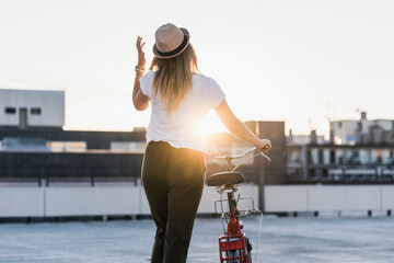 Young woman pushing bicycle on parking level at sunset